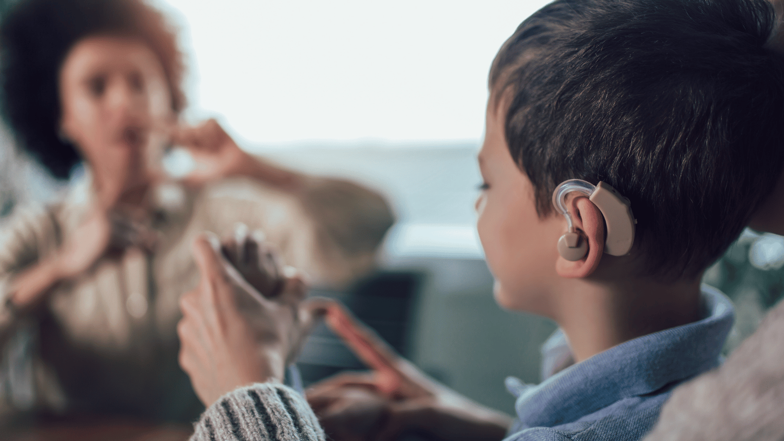 Boy with hearing aid speaking to adult in sign language 