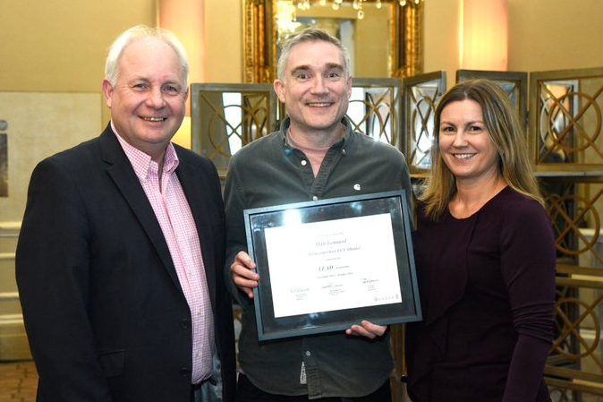 Matt holding graduation certificate with two members of the QuoLux team